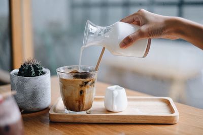 Cropped image of hand pouring tea cup on table