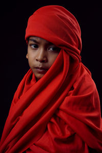 Portrait of boy wearing red textile against black background