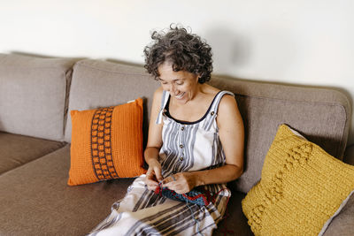 Smiling woman knitting while sitting on sofa at home