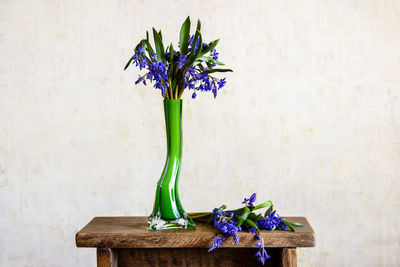 Blue wildflowers in green glass vase on small old handmade wooden table, spring bouquet. copy space.