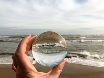 Close-up of hand holding crystal ball against sea