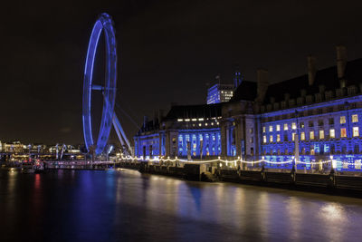 Illuminated london eye by thames river against sky at night