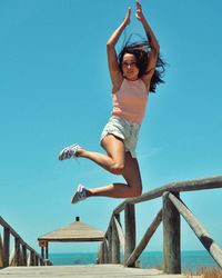 Low angle view of woman jumping against clear blue sky