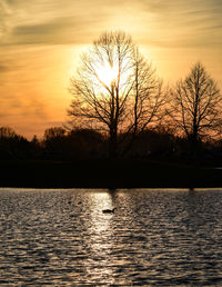 Silhouette bare tree by lake against romantic sky at sunset