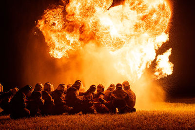 Firefighters crouching on land by fire at night