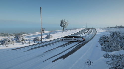 Snow covered road by trees on field against sky