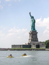 People jet skiing in sea by statue of liberty against sky