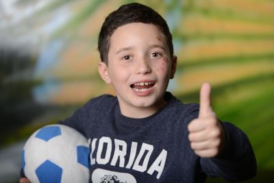 Portrait of boy gesturing thumbs up while holding soccer ball
