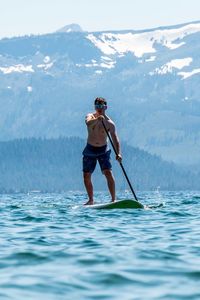 Full length of man paddleboarding in sea against mountain