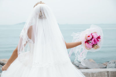 Rear view of bride with bouquet standing against sea