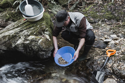 High angle view of man washing rocks in container by stream