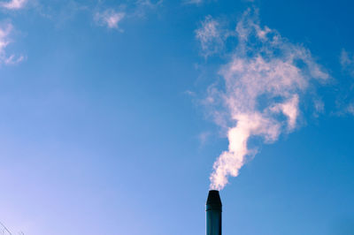 Low angle view of smoke emitting from chimney against blue sky