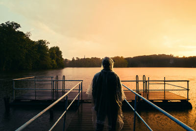 Rear view of man standing on pier over lake during sunset
