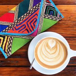 Directly above shot of cappuccino by colorful clutch bag on table in cafe