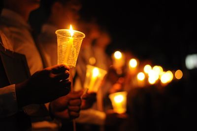 Close-up of people holding lit candles at night