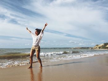 Young woman standing with arms raised on shore at beach during sunny day