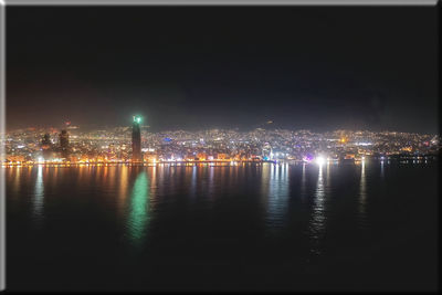 Illuminated buildings by river against sky at night