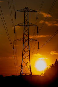 Low angle view of silhouette electricity pylon against sky during sunset