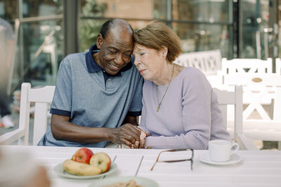 Senior man and woman holding hands while sitting at dining table