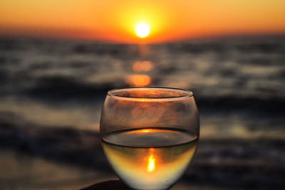 Close-up of beer glass against sea during sunset