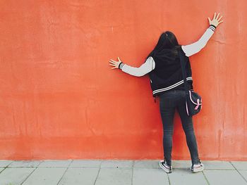 Rear view of woman on sidewalk leaning on orange wall