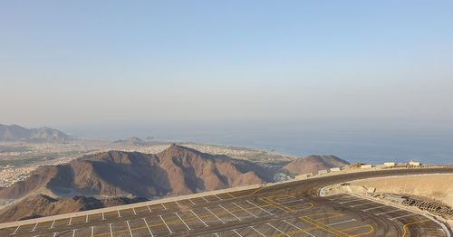 High angle view of parking area against mountains and clear sky above sea in khorfakkan uae. 
