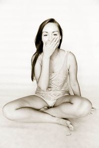 Portrait of woman with hands covering mouth sitting against white background
