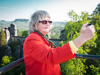 Side view of woman with arms raised standing against sky