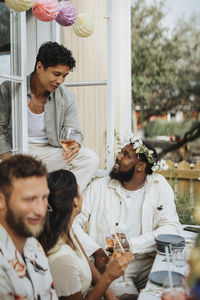 Man holding wineglass while talking to male friend during dinner party at cafe