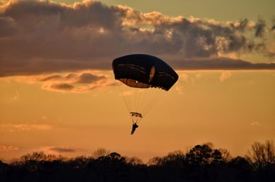 Silhouette of person paragliding against sky during sunset