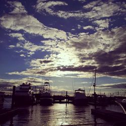 Boats in harbor against cloudy sky