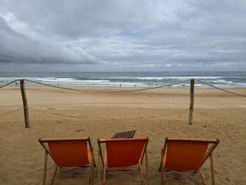 Three orange deck chairs on a sandy beach facing the sea. 