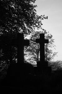 Silhouette of cross at cemetery against sky