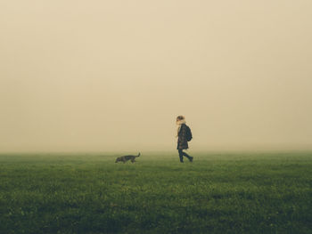 Man with dog standing on field against clear sky