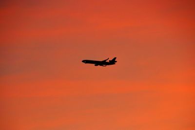 Low angle view of silhouette airplane flying against orange sky