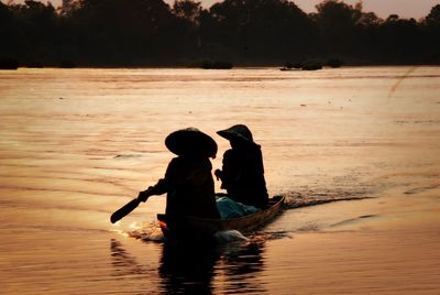 Silhouette people sailing boat in lake during sunset