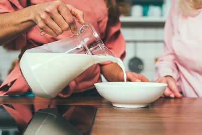 Midsection of woman pouring milk in bowl