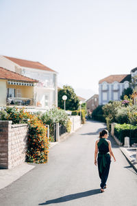 Woman walking by building against clear sky