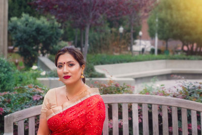 Portrait of confident beautiful woman sitting on bench in garden