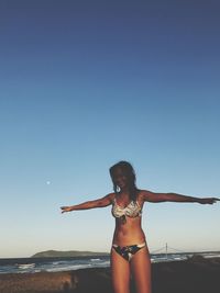 Smiling woman standing with arms outstretched at beach against sky