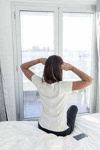 Rear view of woman sitting on bed at home