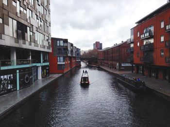 Canal amidst buildings against cloudy sky