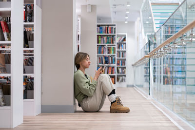 Middle aged student woman sitting on floor reading book in university library. second degree.