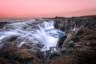 Scenic view of rocks and water fall against sky during sunset