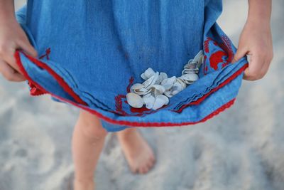 Low section of girl collecting shells in dress