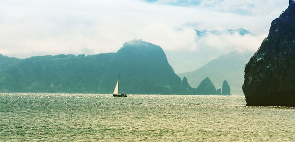 The sailing yacht on the background of the misty sea and rocks