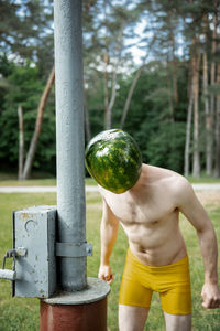 Full length of shirtless man standing by tree