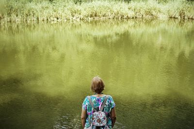 Rear view of senior woman with backpack looking at lake while standing in forest