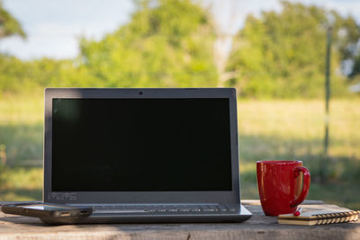 Close-up of laptop with coffee mug on table outdoors