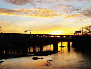 Silhouette bridge over river against sky during sunset